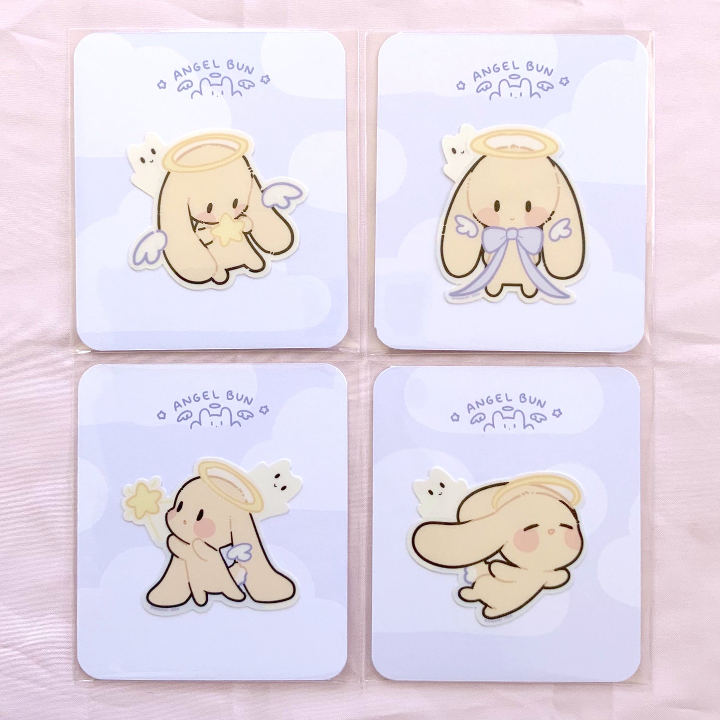 Four cute cartoon angel designs, on a light blue card backing, each sticker is in it's own polybag. photographed on a light pink background