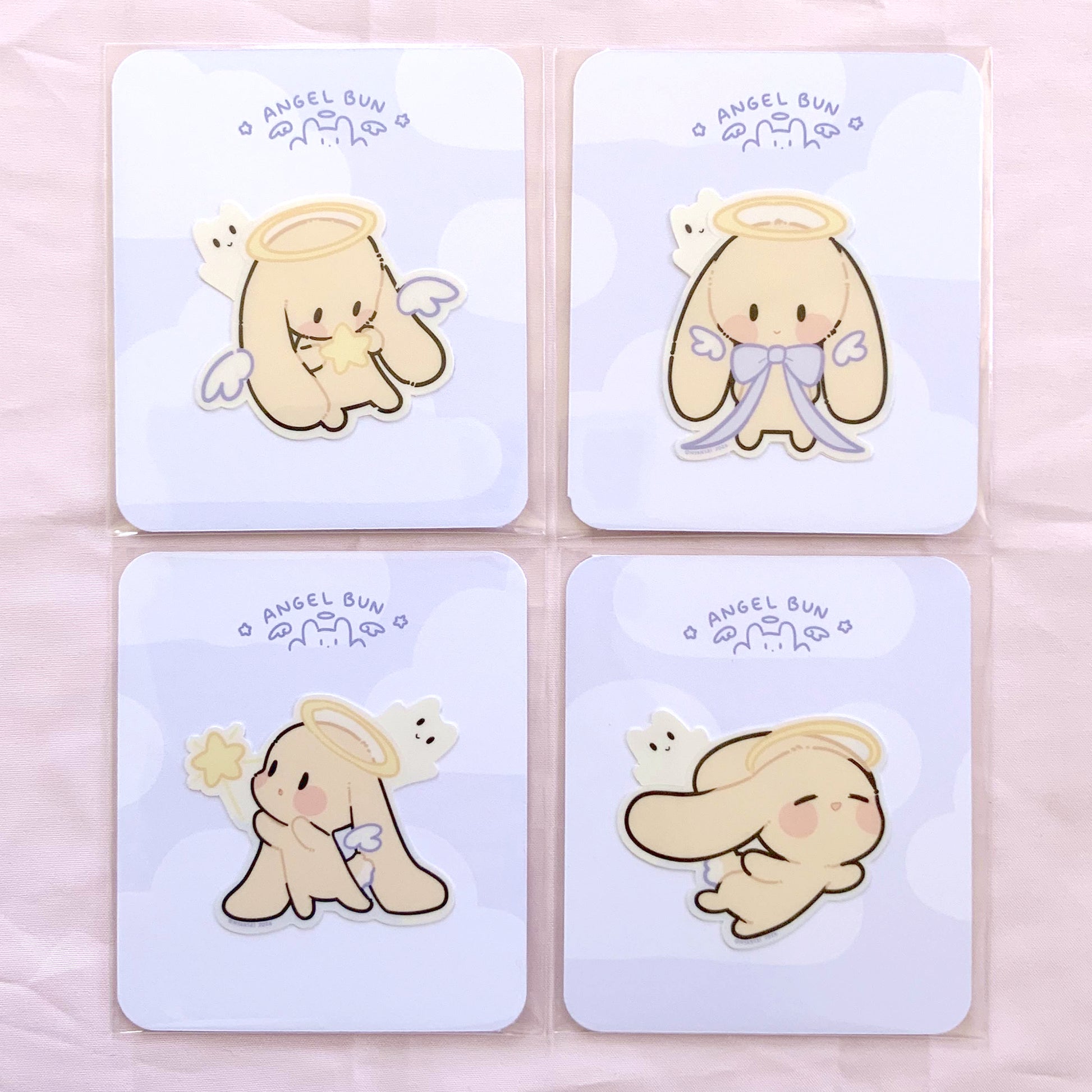 Four cute cartoon angel designs, on a light blue card backing, each sticker is in it's own polybag. photographed on a light pink background