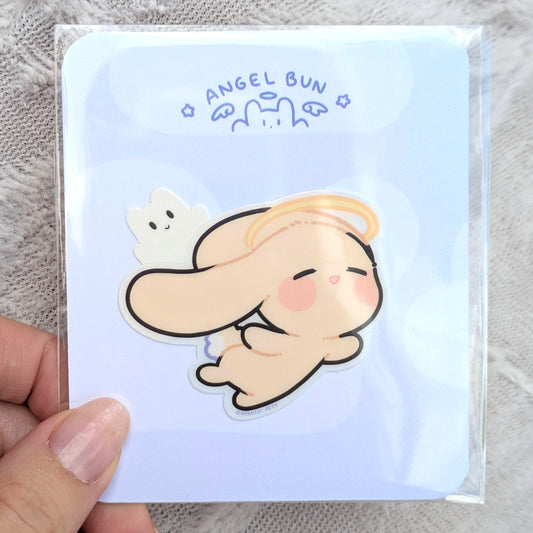 Card with a cute illustration of an angel bunny on a light blue background card, inside of a polybag, being held.