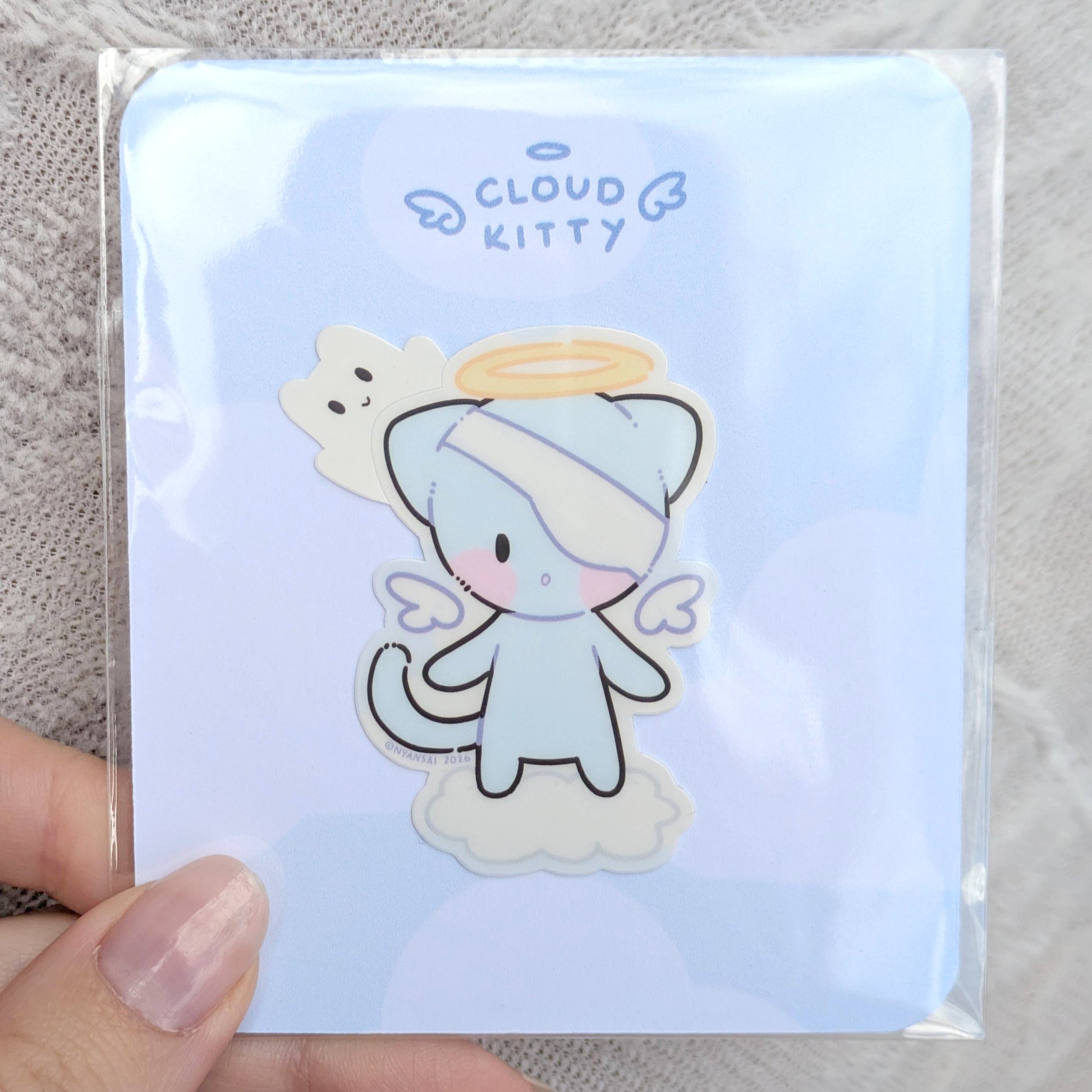 Cartoon cat character on a light blue card with 'Cloud Kitty' text, inside of a polybag, held by a hand.